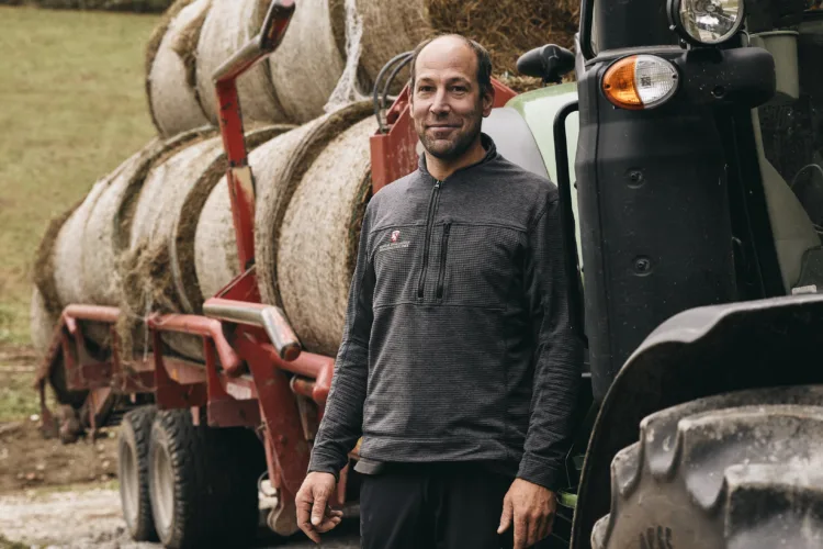 Mann neben Traktor und Heuballen